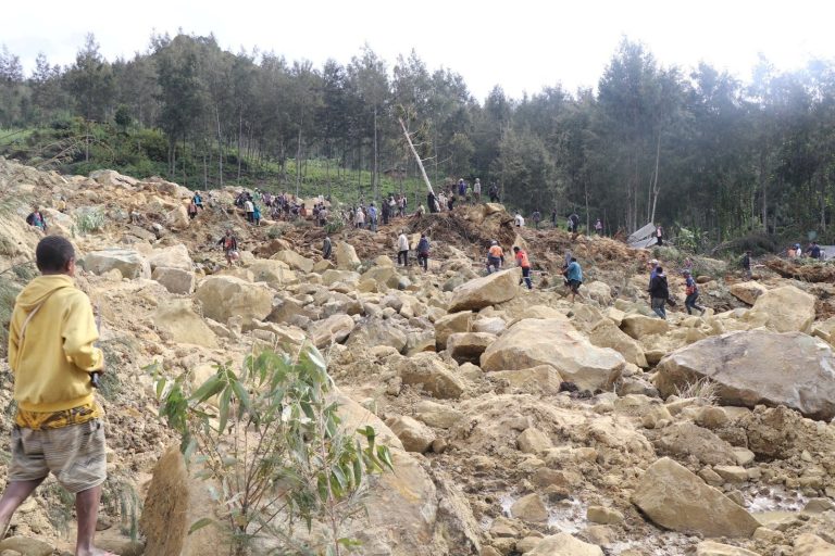 Relief workers and people walk at a site damaged in the aftermath of a landslide in Enga Province