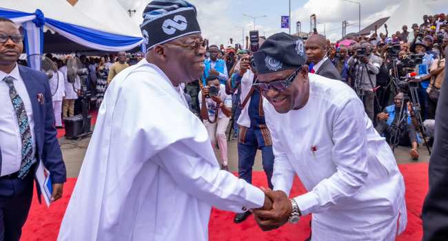 Group Demands Wike’s Dismissal Over Attack On Ijaw People President Tinubu and FCT Minister Nyesom Wike in a warm handshake during an event.